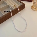 Detailed shot of a delicate white baroque pearl necklace with a gold clasp on a table - White 6mm Pearl Necklace