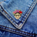 Detailed close-up of a Frida Kahlo enamel brooch on a denim jacket pocket edge - Frida Kahlo Portrait