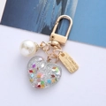 Sparkly resin heart keychain with bell and pearl charm on a minimalist blue background - Clear