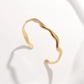 Detail of a gold wavy open cuff bracelet featuring a minimalist lava style design - Gold