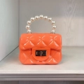 Close-up of an orange mini jelly bag with quilted texture and a white pearl handle - Orange