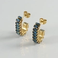 Detail of gold hoop earrings with rectangular blue zircon stones on white surface - Gold With Blue Zirconia