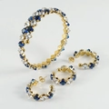 Dettaglio di parure dorata con pietre di zircone blu e bianche a taglio quadrato su fondo bianco - Bianco e Blu