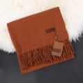 Folded brown cashmere scarf with tassels and leather tag on white faux fur background - Caramel color