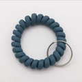 Detail of a matte grey-blue spiral telephone wire wristband with a silver metal key ring - Teal