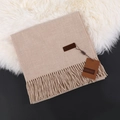 Elegant beige cashmere scarf with fringe and leather brand label on faux fur mat - Oatmeal