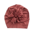 Detail view of brick red ribbed baby turban hat with a large textured floral accent - Rust red