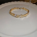 Bracciale dorato a fibbia con zirconi scintillanti presentato su un piatto di porcellana - Bracciale a Doppio Strato Con Fibbia a Cintura