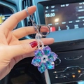 Détail d'un porte-clés fleur en cristal violet tenu à la main à l'intérieur d'une voiture - Violet