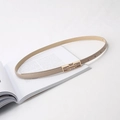 Détail d'une fine ceinture en cuir beige avec boucle en métal doré sur fond blanc - Abricot