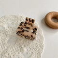 Detail view of a leopard print acetate hair claw clip resting on a beige lace mat - Light Leopard