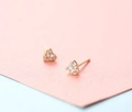Minimalist gold heart stud earrings set with three clear zircons on pink background - Triple Stone Heart