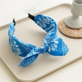 Close-up of blue paisley pattern knotted headband with bow detail on a beige tray - Blue