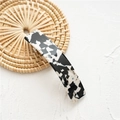 Detail view of marble pattern acetate spring hair clip on a woven lifestyle prop - Acetate Black Marble