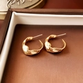 Dettaglio ravvicinato di orecchini a nodo dorati in una lussuosa scatola marrone - Superficie curva geometrica irregolare (1# Silver Earring Post-Oro)