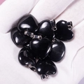 Polished black agate heart pendants with silver bails held in a gloved hand - Obsidian