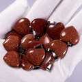 Brown goldstone heart pendants with metal bail clasps held in hand closeup - Gold Sandstone