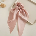 Close-up of pink satin scrunchie with long ribbons on a minimalist wood display - Pink