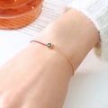 Bracciale in corda rossa con mezza catena d'oro e pietra scura sul polso di una modella - Gennaio Nero