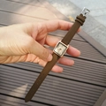 Square rose gold watch with brown strap and numeric dial shown held in hand - Coffee
