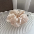 Macro view of champagne satin hair scrunchie with rhinestones on a glass tray - Apricot