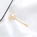 Dettaglio di un fermaglio per capelli dorato con perla a forma di cuore su seta bianca - Cuore