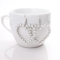 Elegant silver heart-shaped pearl drop earrings hanging on a white ceramic cup - Silver