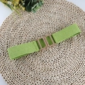 Close-up of green woven elastic belt with golden interlocking rectangular buckle on straw mat - Green