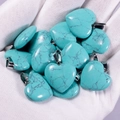 Natural heart-shaped turquoise stone pendants with metal bails held in a hand - Turquoise Howlite