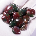 Polished natural agate heart pendants with red and green patterns held in hand - India Agate