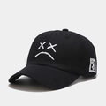 Primer plano de gorra de algodón negro con bordado de cara triste y detalle en el lateral - Ajustable / Negro