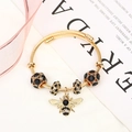 Detail of a gold bee pendant and black rhinestone beads on a steel wire bracelet - Gold Black