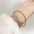 Minimalist gold plated titanium steel bangle shown on a wrist with white textured cuff - Gold / M