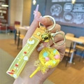 Detail of yellow unicorn liquid sand keychain with lollipop charm and bell in hand - Yellow Luminous Lollipop