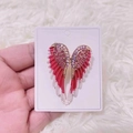 Dettaglio della spilla ad ali di angelo con strass rossi su cartoncino da esposizione - Rosa