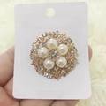 Dettaglio della spilla a fiore dorata con cinque perle bianche e strass scintillanti - Fiore a 5 petali traforato