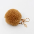 Dettaglio portachiavi in peluche marrone con ciondolo a foglia dorata e perla su sfondo bianco - caffè