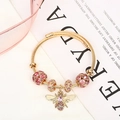 Macro detail of golden twist bracelet featuring pink crystal beads and a honey bee charm - Gold Pink