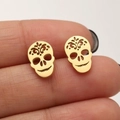 Gothic gold skull stud earrings with intricate hollow patterns shown on a fingertip - Gold