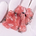 Pink strawberry quartz drop pendants with metal clasps held on a gloved palm - Watermelon red