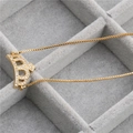 Dettaglio macro di una collana con ciondolo a corona dorata e zirconi su vassoio in velluto - Corona B (Zirconia Bianca) / Oro