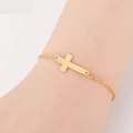 Close-up of a minimalist golden cross bracelet on a female wrist with delicate chain link - Cross / Gold