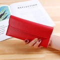 Red long wallet in litchi grain leather with flap closure held against a wooden desk - Red