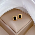 Macro shot of minimalist gold and black square stud earrings on silk background - Gold