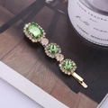 Elegante fermaglio dorato con cristalli verdi e strass posato su una rivista - verde chiaro