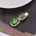 Dettaglio di un fermaglio dorato con gemme verdi e strass brillanti incastonati - verde scuro