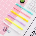 Flat lay of six colorful bamboo-shaped gel pens on a pink grid mat with office accessories - Flute Shape