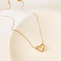 Minimalist gold titanium steel heart pendant necklace displayed on ceramic plate - Gold Hollow Heart