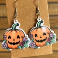 Nahaufnahme von Halloween-Kürbis-Ohrringen aus Acryl mit bunten Blumen auf Holzgrund - Kürbis