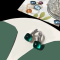 Detailed macro view of silver earrings featuring square emerald green stones and pave crystals - Peacock Blue